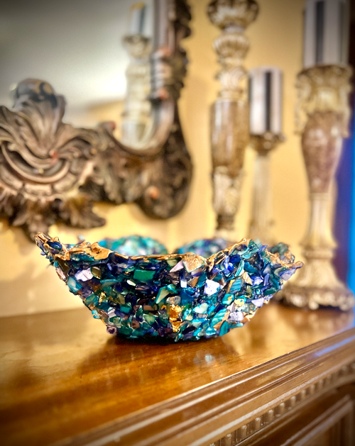 Decorative blue crystal bowl on a wooden surface with ornate candle holders in the background.